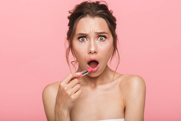 Image of a pretty shocked young woman posing isolated over pink wall background holding lipstick. - Фото, изображение