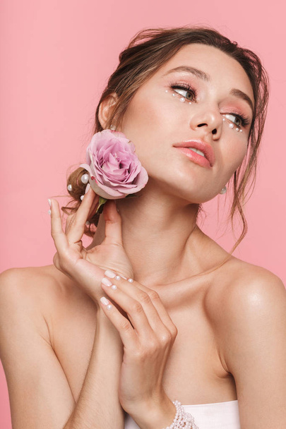 Beauty portrait of an attractive young topless woman posing with a flower isolated over pink background, wearing white pearls - Fotoğraf, Görsel
