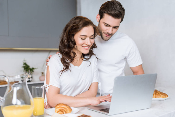 happy couple using laptop near tasty breakfast in kitchen - Zdjęcie, obraz