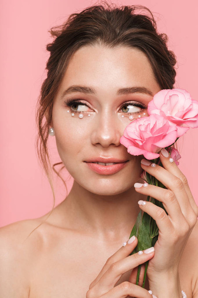 Image of a pretty young woman posing isolated over pink wall background with flowers. - Foto, Imagen
