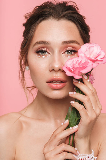 Image of a pretty young woman posing isolated over pink wall background with flowers. - Foto, imagen