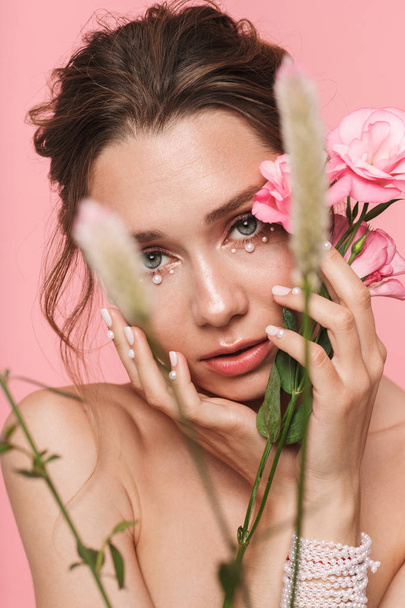 Beauty portrait of an attractive young topless woman posing with a flowers isolated over pink background, wearing white pearls - Foto, afbeelding