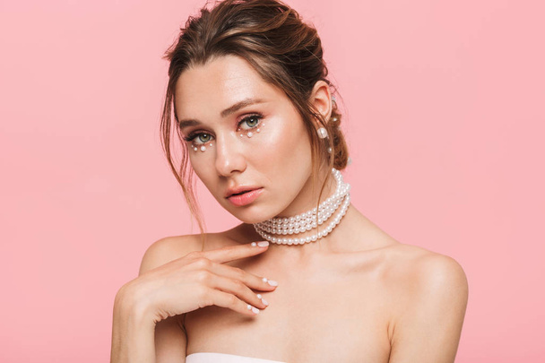 Beauty portrait of an attractive young topless woman posing isolated over pink background, wearing white pearl necklace - Foto, afbeelding