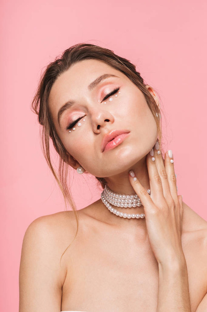 Beauty portrait of an attractive young topless woman posing isolated over pink background, wearing white pearl necklace - Φωτογραφία, εικόνα