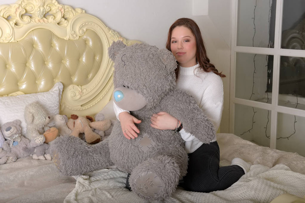 brunette teen girl with big gray bear on the bed - Photo, Image