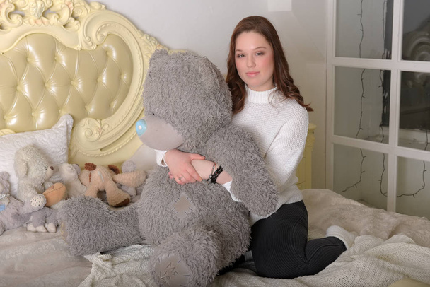 брюнетка дівчина-підліток з великим сірим ведмедем на ліжку
 - Фото, зображення