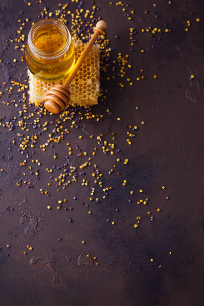 jar with honey, honeycomb and wooden spoon on brown table - Photo, Image