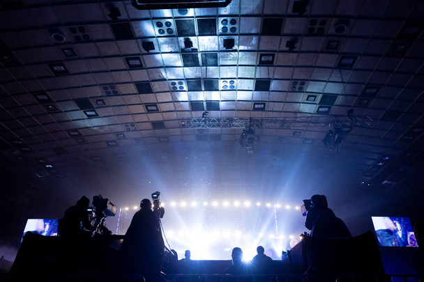 Silhouette of a group of cameramen broadcasting an event. Workers are on a high platform on the background of bright beams. - Photo, Image