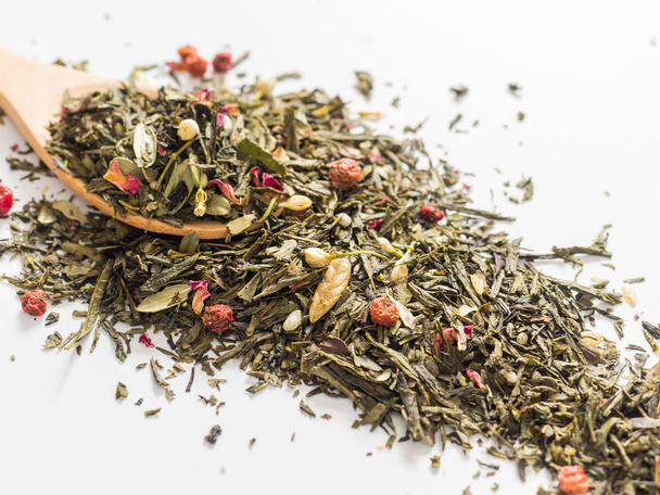 Droge bladeren van Sencha groene bloem thee met bekend blad, rode bessen, jasmijn, roos bloemblaadjes, honing korrels, bos berry aroma op witte achtergrond - Foto, afbeelding