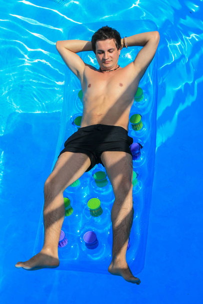 09.25.2008, Hersonissos, Crete, Greece. Travel around Greece. a young man swims on a water mattress in a blue water pool - Φωτογραφία, εικόνα