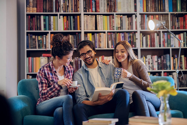 Grupo de três jovens estudantes sentados na biblioteca moderna e fazendo uma pausa da aprendizagem difícil. Preparação dos exames em conjunto
. - Foto, Imagem