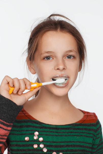 Πορτρέτο ενός οκτώ-έτος-παλαιό κορίτσι που βουρτσίζει τα δόντια της με μια οδοντόβουρτσα. Ριγέ πουλόβερ - Φωτογραφία, εικόνα