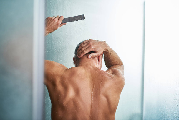 Young man using shower head while washing himself in bathroom - Φωτογραφία, εικόνα