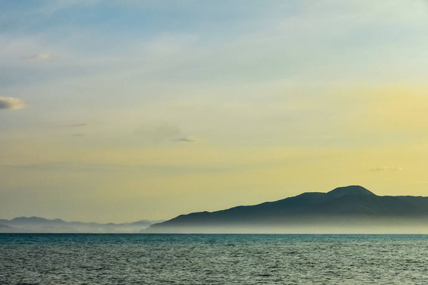 beautiful line of sea and blue-yellow sky. majestic mountains in the fog - Φωτογραφία, εικόνα