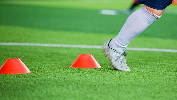 Futbolcu koşu ve futbol eğitim için yeşil suni çim üzerinde koni işaretleri arasında atlamak. Futbol ya da futbol Akademisi. - Fotoğraf, Görsel