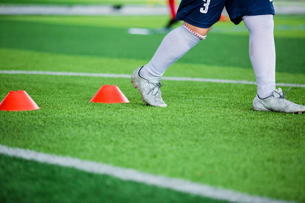 Футболист бег трусцой и прыжки между маркерами конуса на зеленой искусственной территории для футбольных тренировок. Футбольная академия
. - Фото, изображение