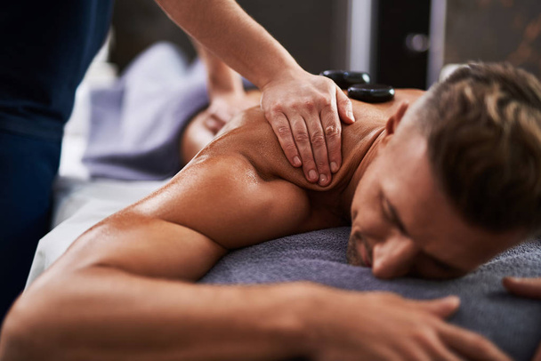 Masseur hands massaging client shoulder while he lying on massage table - Fotografie, Obrázek