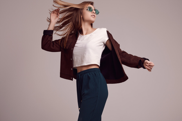 Portrait of cute teenage girl in fashion jacket and color glasses posing on gray background. Studio shoot. - Foto, Imagen