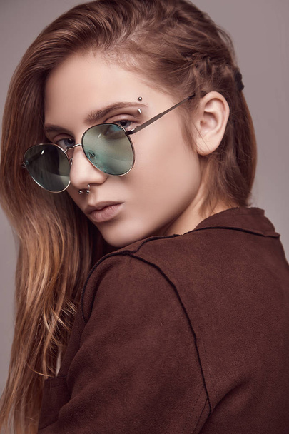 Retrato de linda adolescente en chaqueta de moda y gafas de color posando sobre fondo gris. Sesión de estudio
. - Foto, Imagen