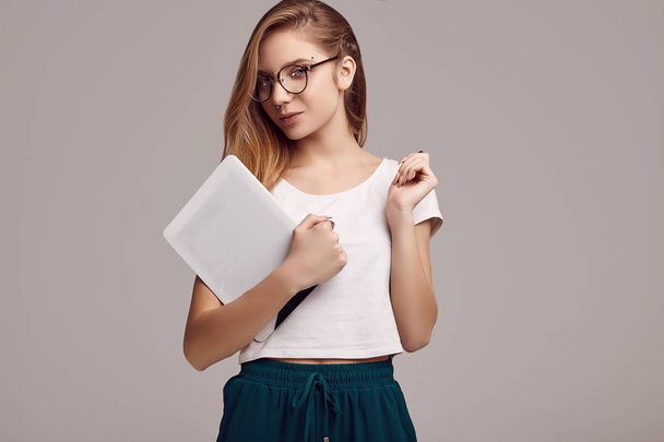 Portrait of cute teenage girl in white shirt and glasses holding digital tablet on gray background. Studio shoot. - Foto, Bild