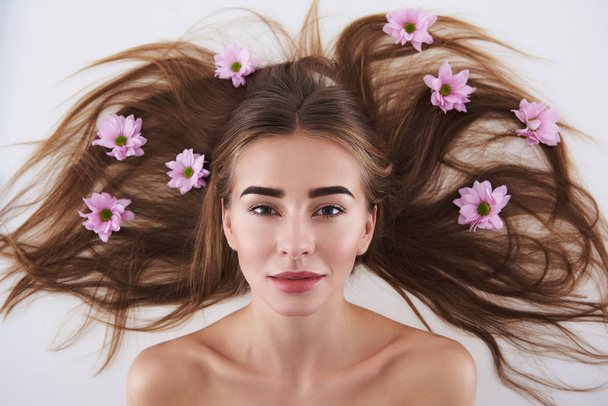 Attractive young lady with flowers in her hair lying on white background - Foto, immagini