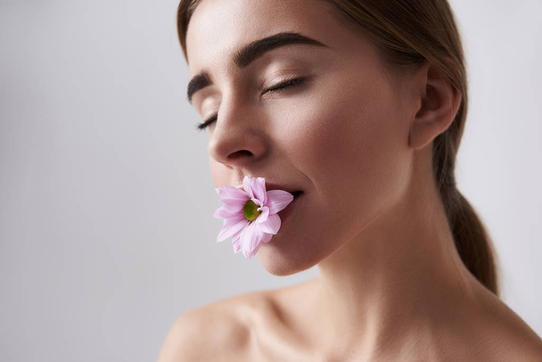 ul young lady with perfect skin holding pink flower in mouth - Photo, Image
