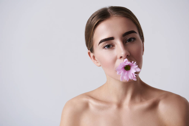 Attractive young woman holding pink flower in mouth - 写真・画像