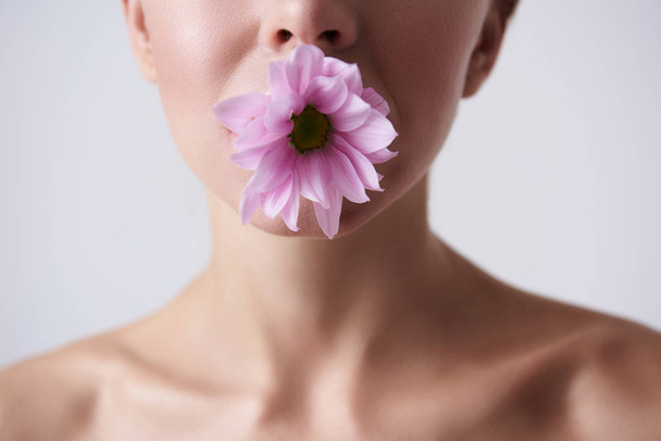 Ağızda hoş pembe çiçek tutan genç kadın - Fotoğraf, Görsel