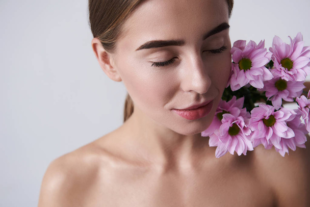 Attractive young woman keeping beautiful pink flowers on naked shoulder - Fotografie, Obrázek