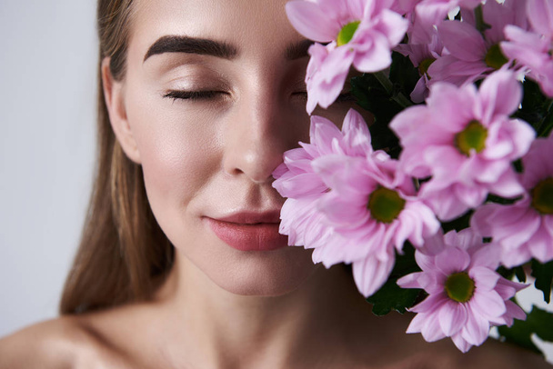 Attractive young woman enjoying aroma of beautiful pink flowers - Foto, afbeelding
