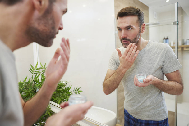 Homem aplicando creme facial em seu rosto no banheiro
 - Foto, Imagem