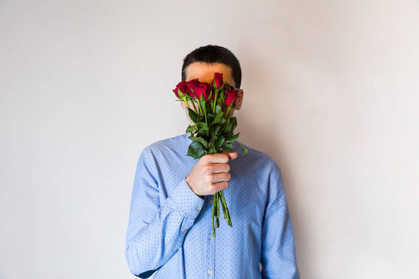 Αστεία έκπληξη για την αγάπη, ρομαντική άνθρωπος κρατώντας κόκκινα τριαντάφυλλα, κρύβονται πίσω από τους. Χαριτωμένο δώρο. - Φωτογραφία, εικόνα