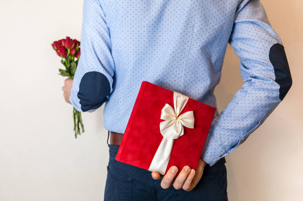 Sorpresa de regalo romántico, hombre ocultando regalo, regalo y sosteniendo rosas rojas, amor de pareja, relación romántica, día de San Valentín, día de la mujer, 8 de marzo
. - Foto, imagen