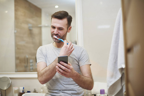 Man brushing his teeth and using mobile phone  - Foto, Imagen