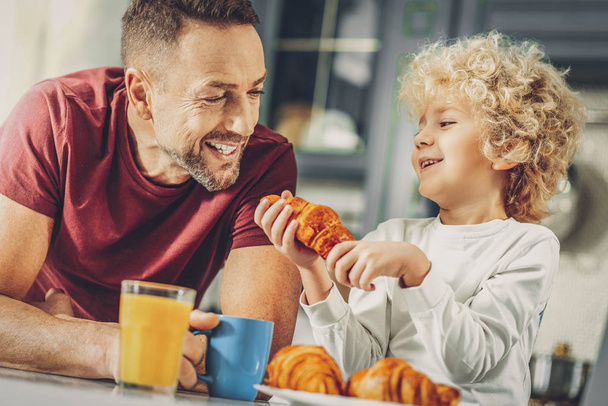Happy merry man and boy eating croissant - Photo, image