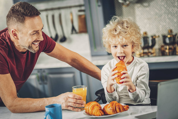 Cunning charming boy enjoying croissant and juice - Foto, afbeelding