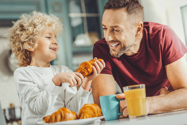 Happy father and son eating tasty croissants for breakfast - Фото, изображение