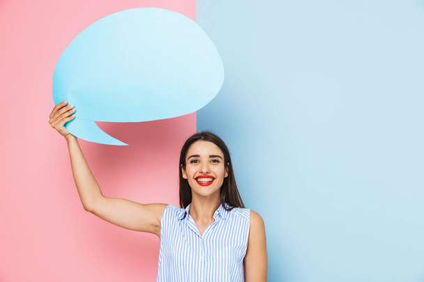 Cheerful young woman standing isolated over two colored background, holding empty speech bubble - Фото, зображення