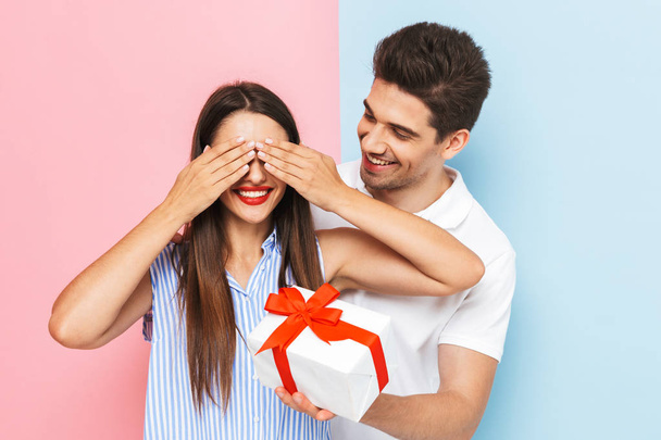 Happy young couple standing isolated over two colored background, celebrating, holding gift box - Фото, изображение