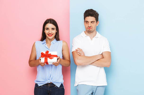 Happy young couple standing isolated over two colored background, celebrating, holding gift box - Φωτογραφία, εικόνα