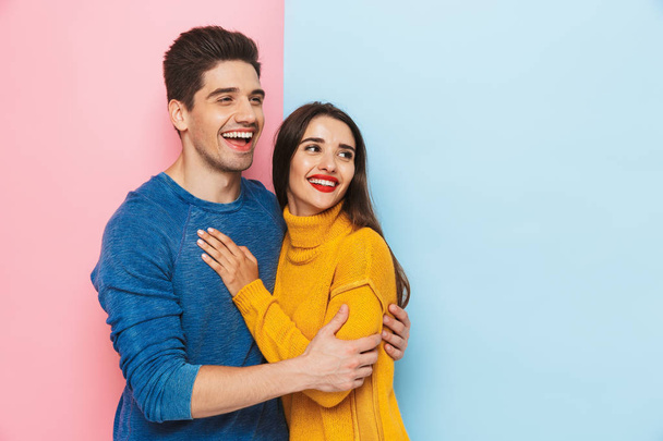 Cheerful young couple standing isolated over two colored background, hugging - Фото, зображення