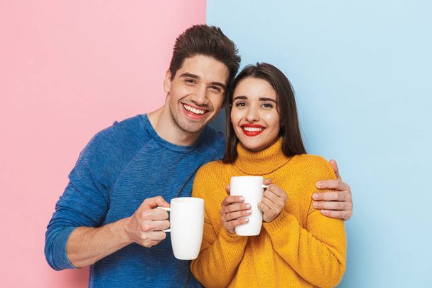 Beautiful young couple standing isolated over two colored background, holding cups with tea - Foto, Bild