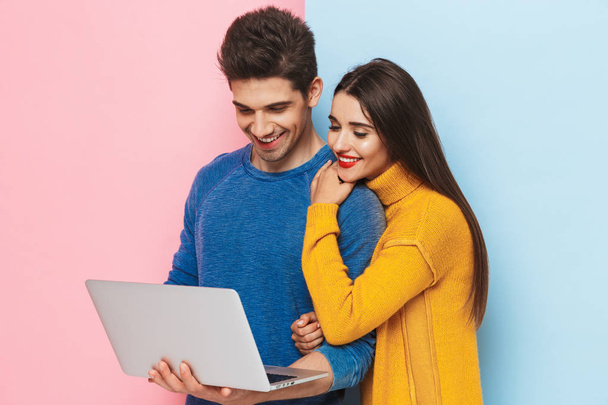 Beautiful young couple standing isolated over two colored background, using laptop computer - Foto, Imagen