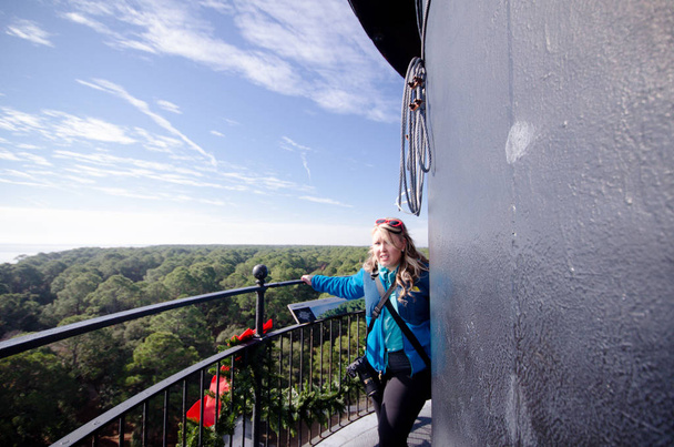 Scared blonde adult woman with a fear of heights hangs on to the railing climbing the spiral staircase to top of Hunting Island Lighthouse in South Carolina - Photo, Image