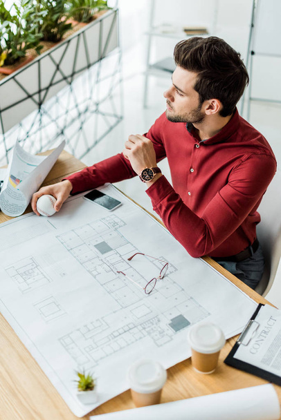 handsome male architect sitting and working on blueprint in office - Photo, Image