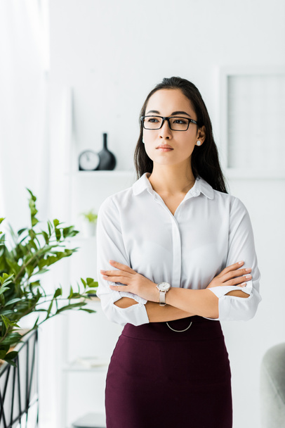 hermosa confiada asiática mujer de negocios en formal desgaste y gafas con brazos cruzados en oficina
 - Foto, Imagen