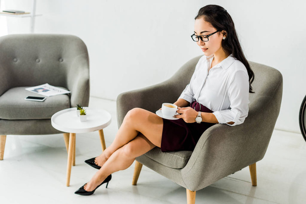 belle asiatique femme d'affaires assis sur fauteuil avec tasse de café au bureau
  - Photo, image