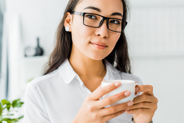 attractive asian businesswoman in glasses having coffee break in office - Photo, Image
