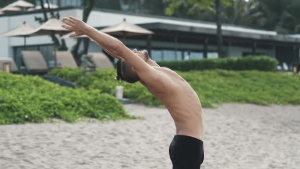 Young athletic man practicing yoga exercise and pulls his hands up - Video
