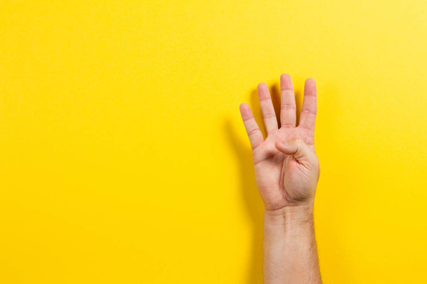 Ο άνθρωπος χέρι δείχνοντας τα τέσσερα δάχτυλα σε κίτρινο φόντο. Αριθμός δύο σύμβολο - Φωτογραφία, εικόνα